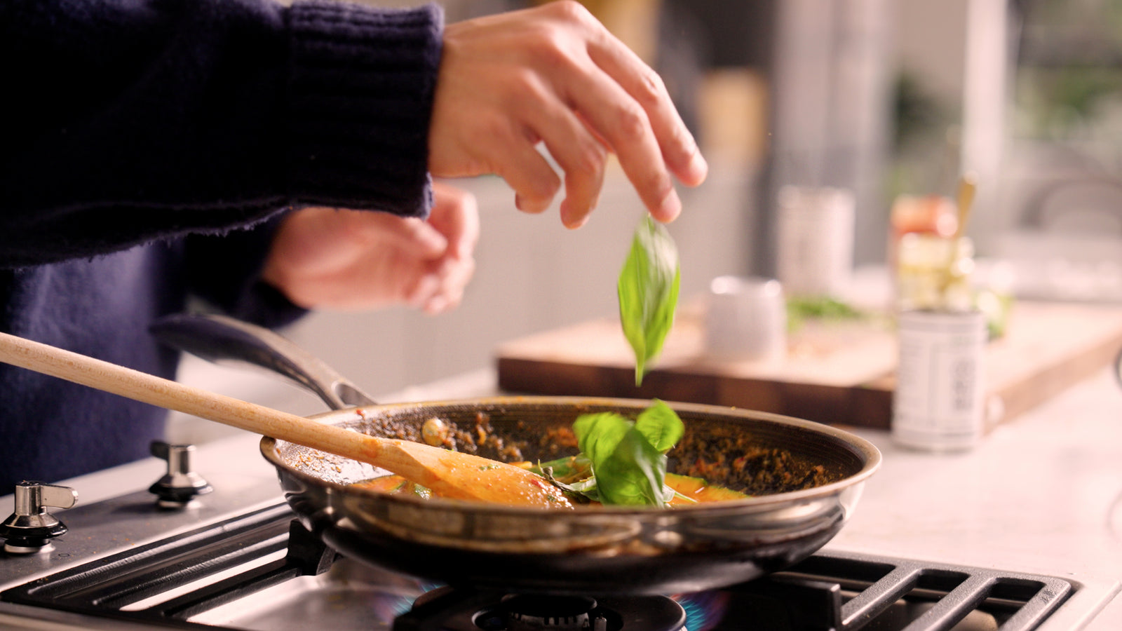 Fresh Thai basil being added to a curry cooking in a pan